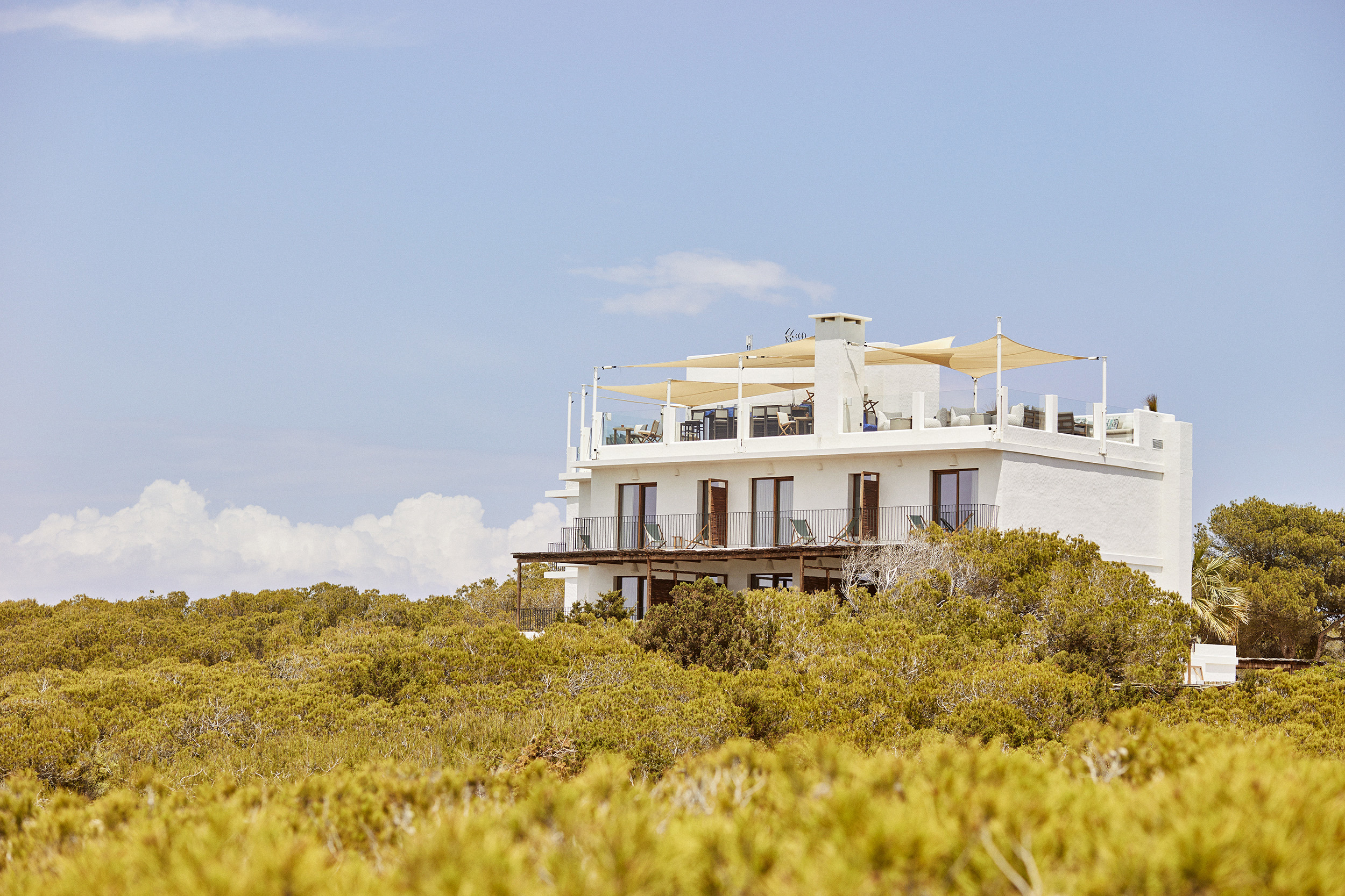 The whitewashed exterior of Teranka hotel surrounded by shrubbery under a clear sky