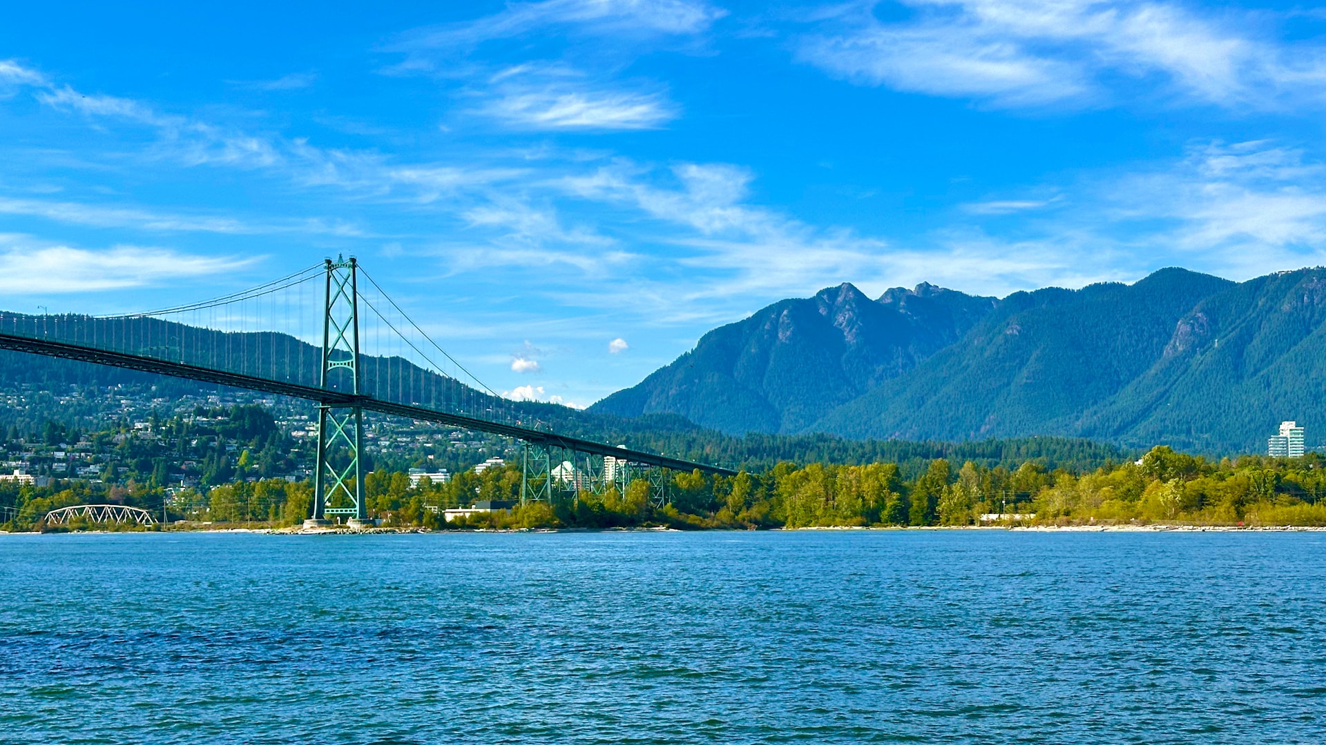 The Lions Gate suspension bridge spans across a river in Vancouver with a mountainous landscape in the background